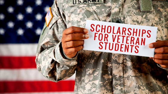 US military personnel holding a sign reading scholarships for veteran students. The person is standing in front of an American flag backdrop.